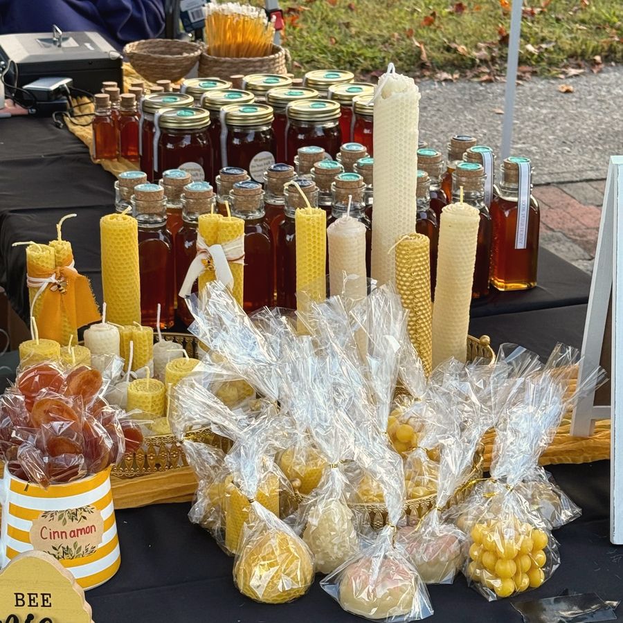 Hand-rolled beeswax taper candles, honey bottles and honey suckers on a market table, Honey Tree Orchard & Apiary